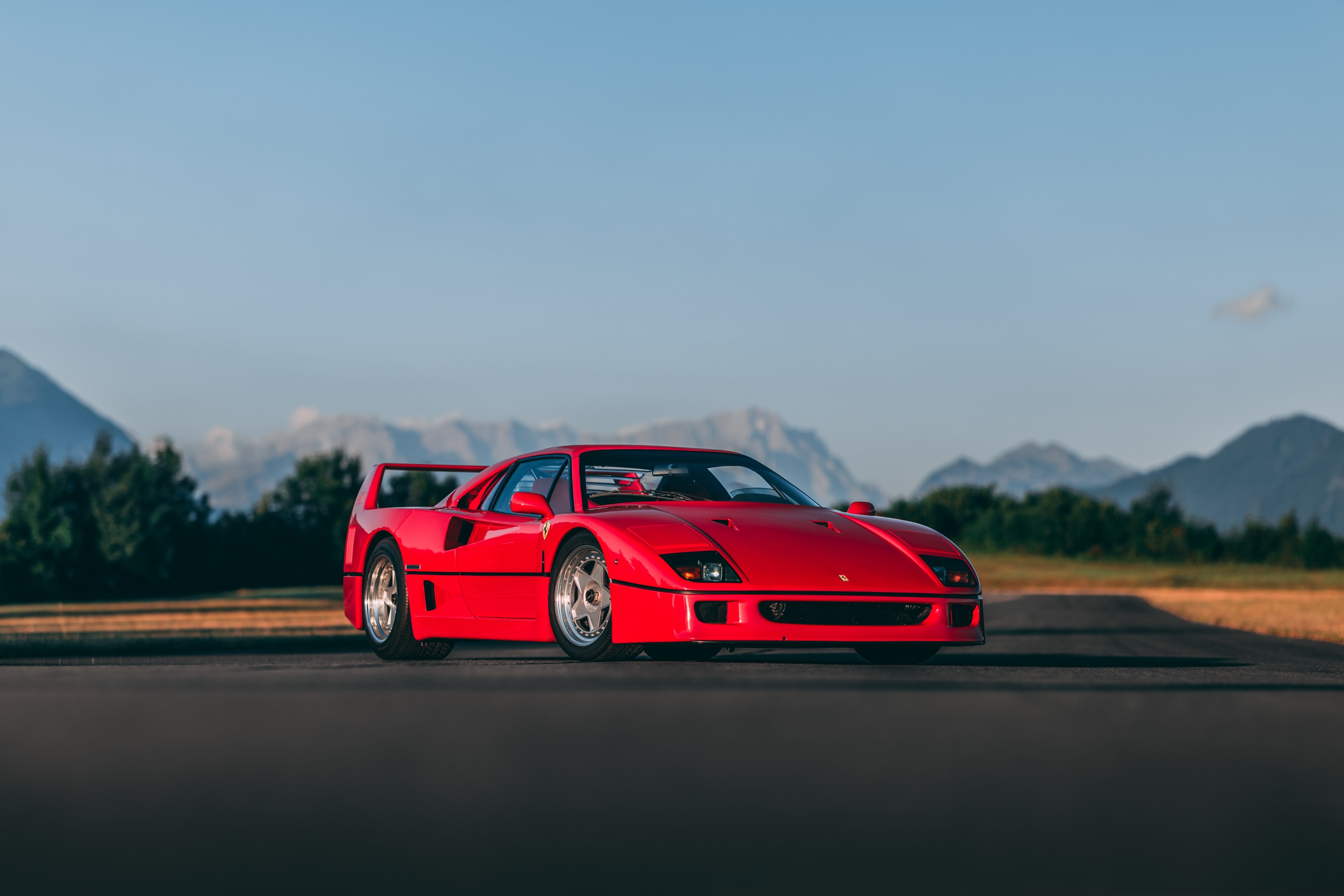 Red Ferrari F40 on an airstrip at golden hour, with the Alps in the background
